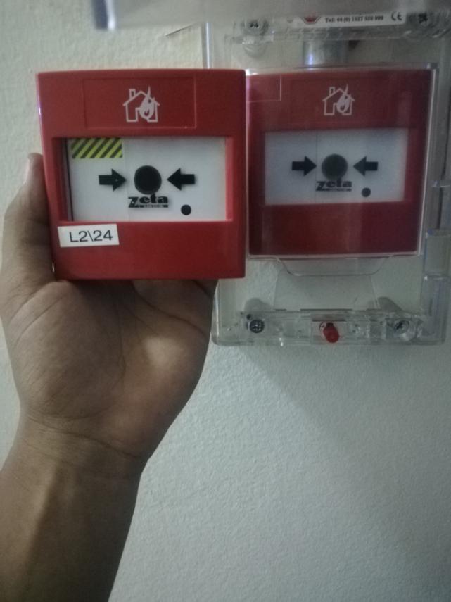 Technician presenting a replaced fire alarm call point at an ABO site